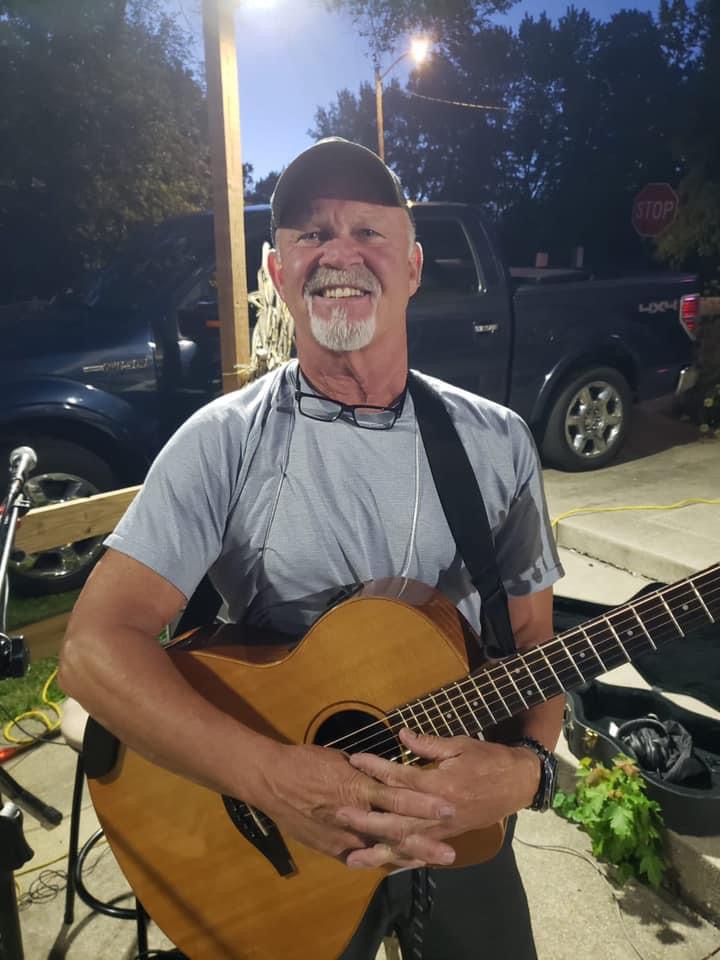 Chad Hinsenkamp smiling at the camera with his acoustic guitar